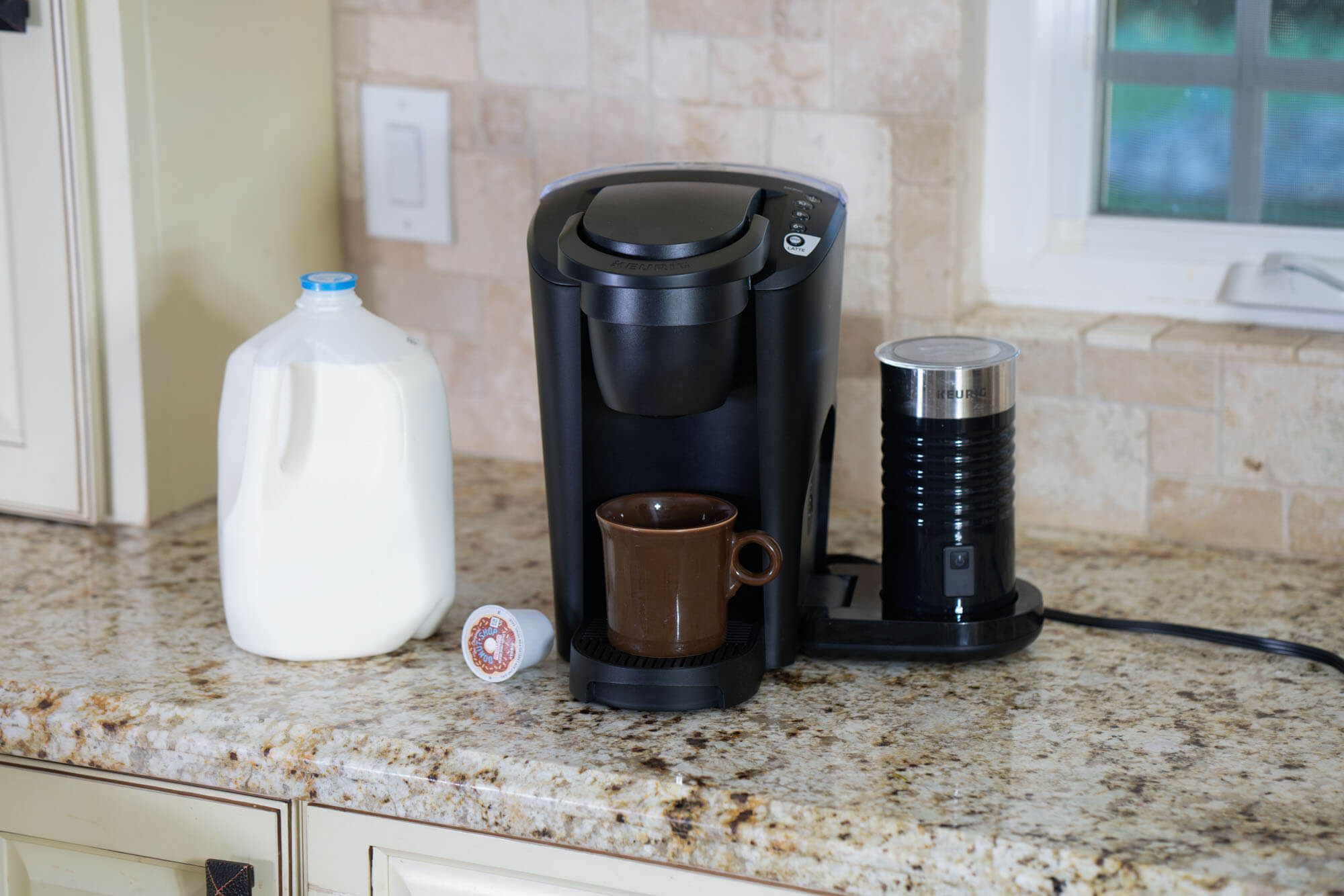 Latte machine on granite countertop with milk next to it. 